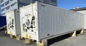 To store, hvite kjølecontainere, merket "Thermo King", fungerer som et midlertidig fryselager, hevet opp på treklosser utendørs på en solrik dag.